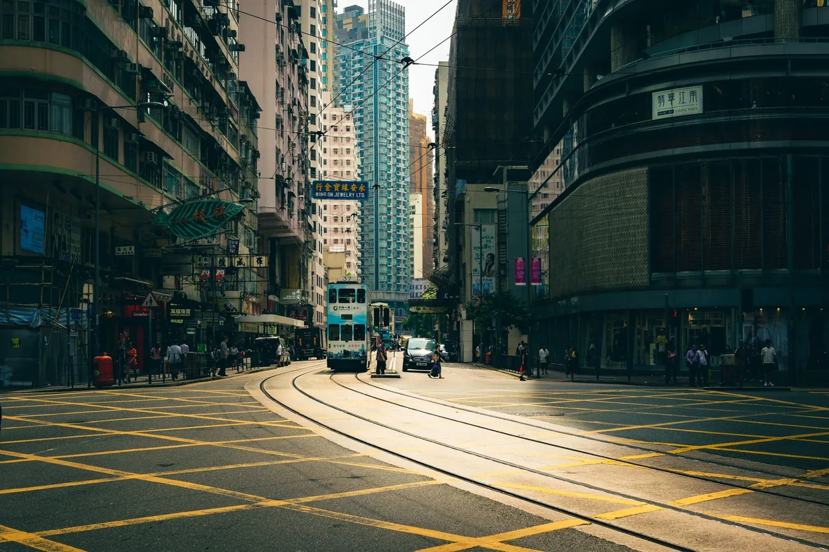 香港港岛街头的电车路口：一辆双层电车沿弯道驶来，路面画着黄色方格线，两旁是高楼
